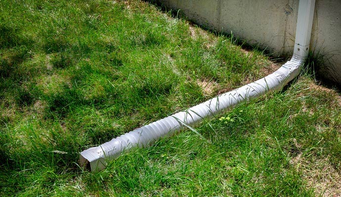A flexible gutter downspout extension running across a green grass lawn