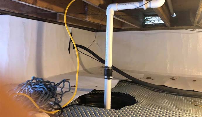 Sump pump basin with vertical PVC discharge pipe installed in an encapsulated crawl space