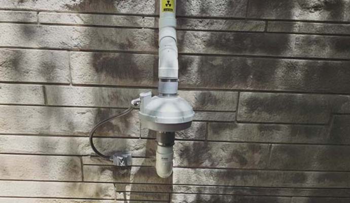 Exterior radon mitigation fan and PVC pipe installed on an exterior stone wall