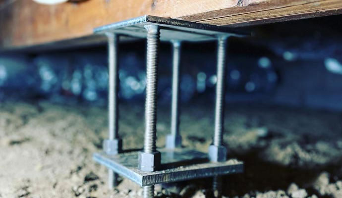 An adjustable metal support post stabilizing a wooden beam in a crawl space