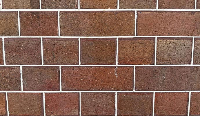A detailed view of a red and brown brick wall with white mortar