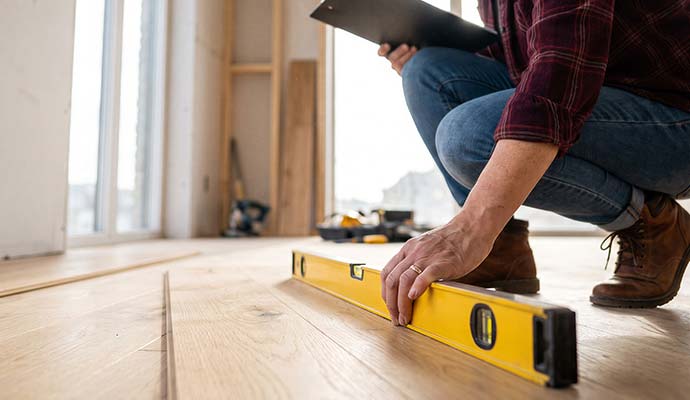 Technician using a yellow spirit level to check the slope of a wooden floor