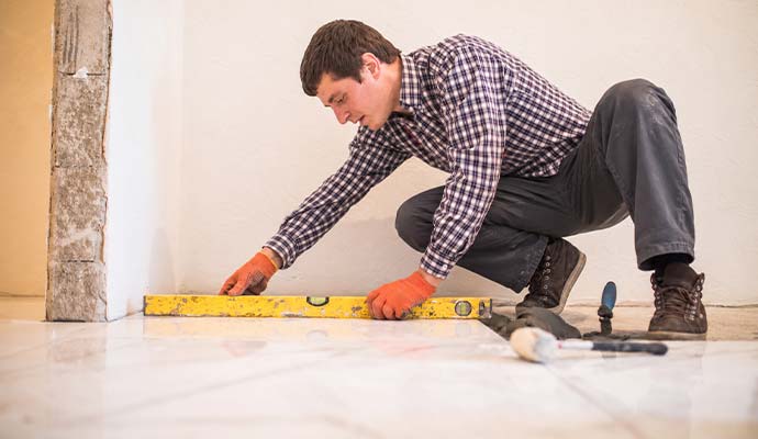 Technician in work gloves using a spirit level to check the alignment of floor tiles