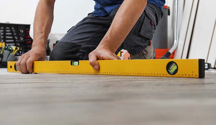 Worker placing a long yellow spirit level on a floor to check for unevenness